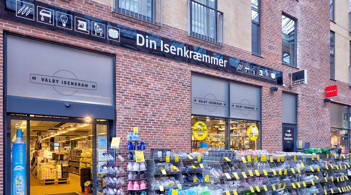 Facade af Valby Isenkram med udstilling af køkkenudstyr og husholdningsartikler udendørs.