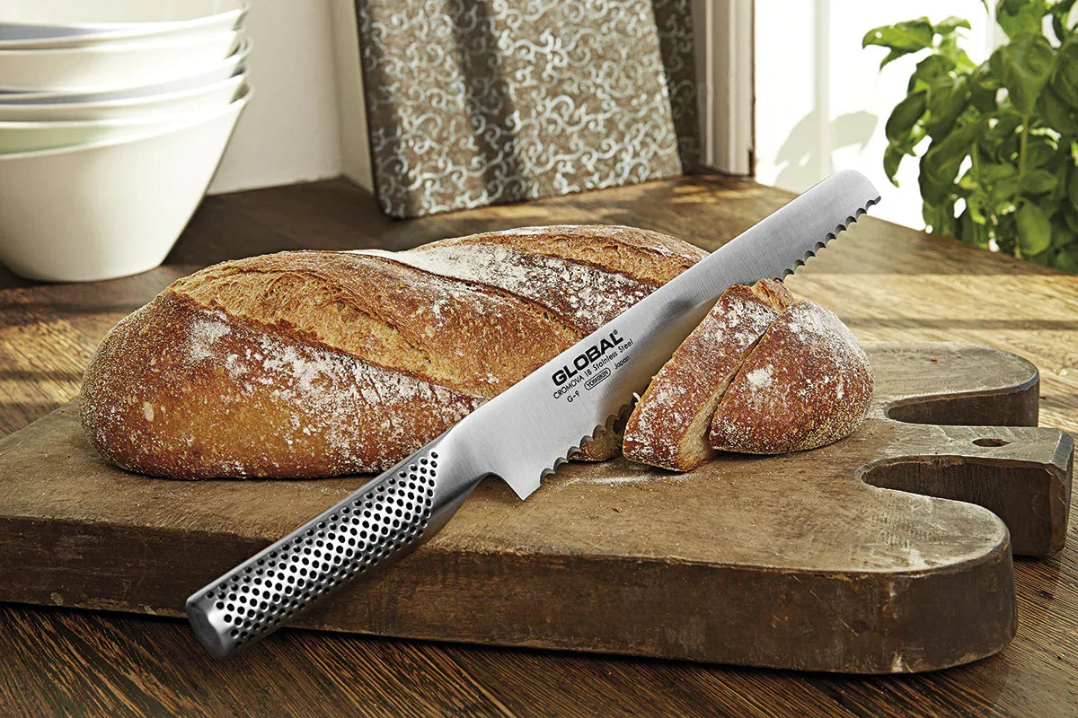 GLOBAL brødkniv G-9 placeret på et skærebræt ved siden af et friskbagt brød