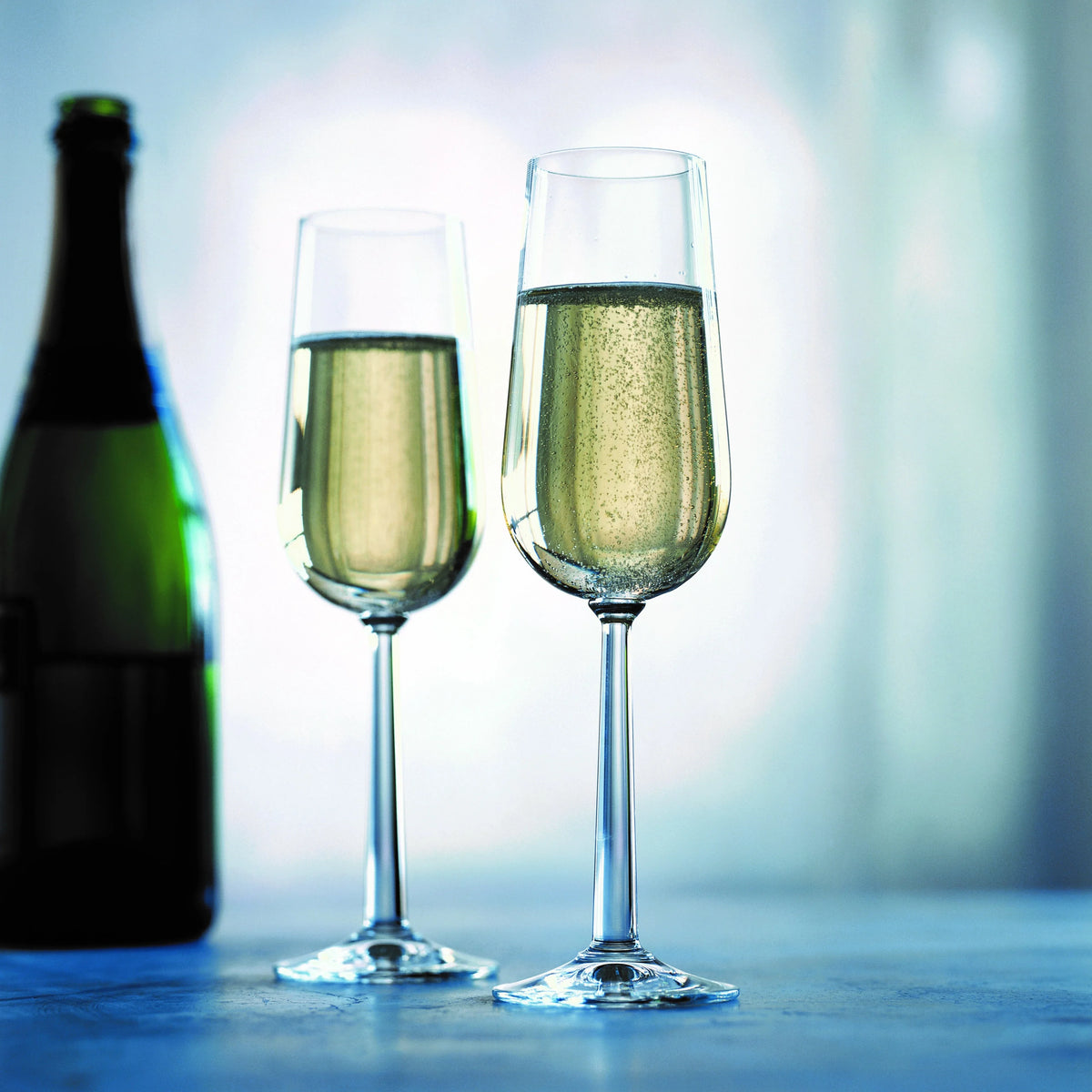 To ROSENDAHL Grand Cru champagneglas fyldt med bobler ved siden af en champagneflaske.