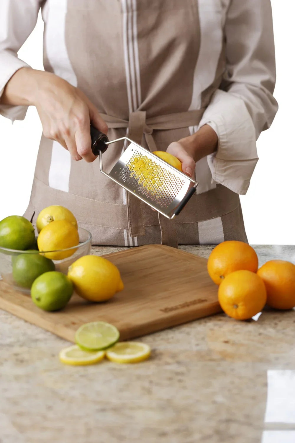 Person der bruger et MICROPLANE rivejern til at rive citronskal over et skærebræt med citrusfrugter