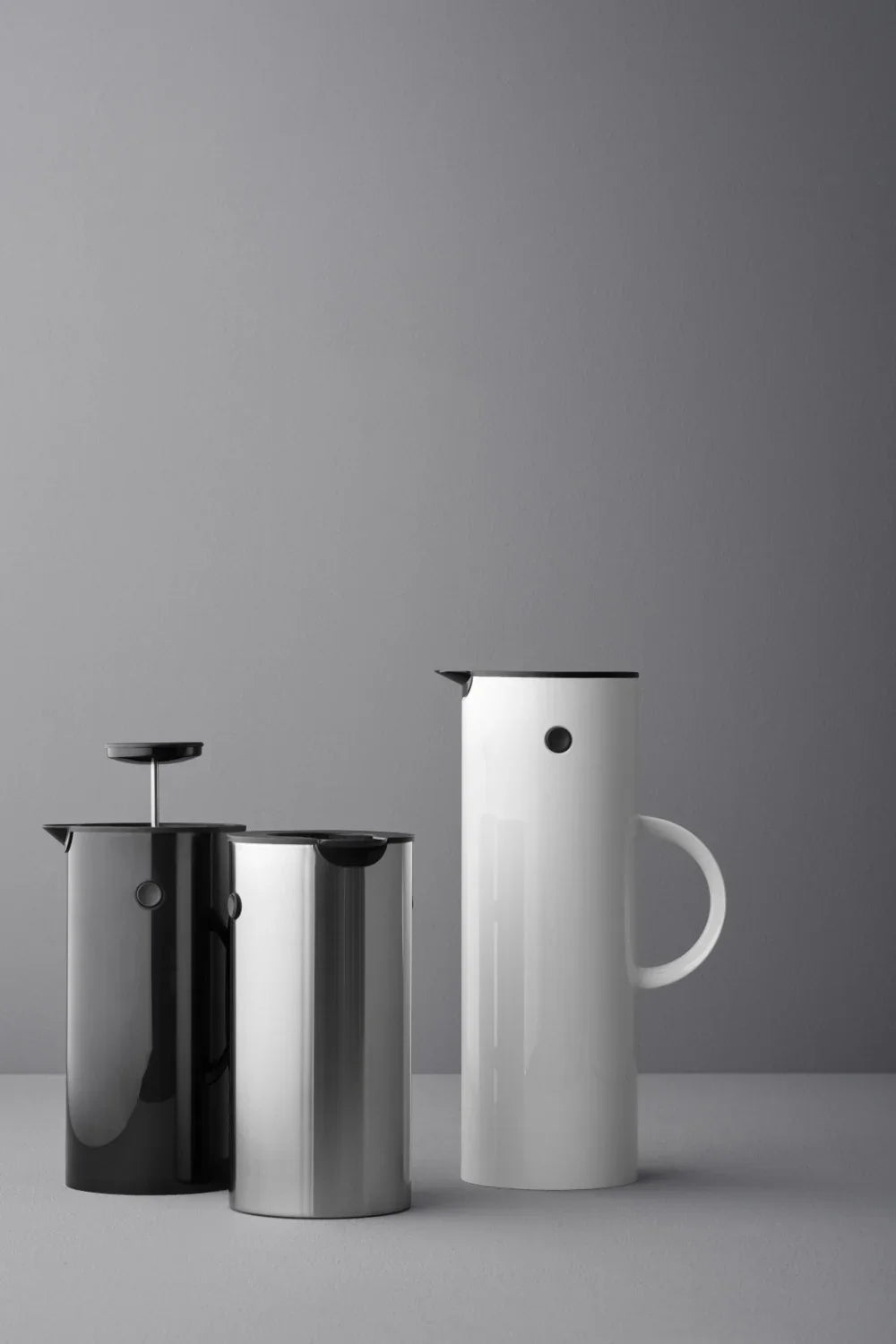 Tre STELTON stempelkander i sort, sølv og hvidt design mod en grå baggrund.