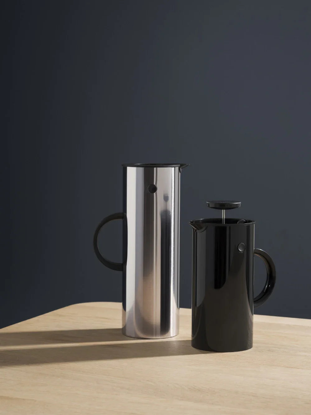 To STELTON stempelkander i sort og rustfrit stål på et lyst træbord.