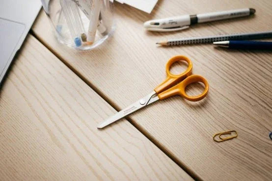 Fiskars hobbysaks med orange håndtag på et lyst træbord med skriveredskaber