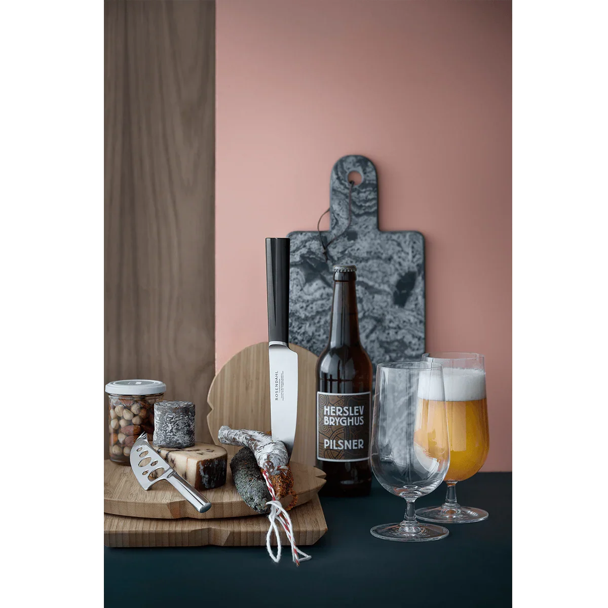 To ROSENDAHL Grand Cru ølglas med pilsner, ølflaske og snacks på et træskærebræt.