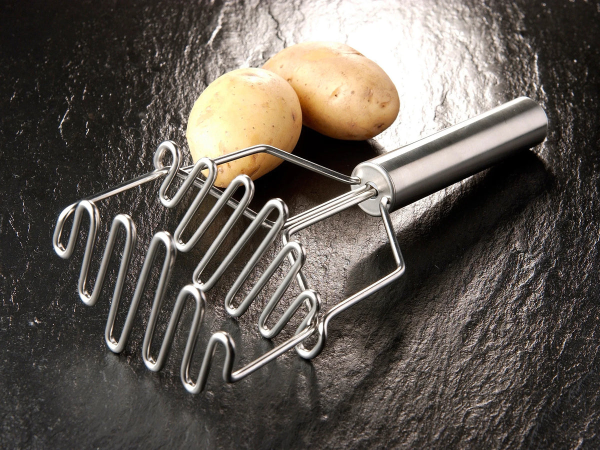 FUNKTION kartoffelmoser i rustfrit stål med fjedermekanisme ved siden af to rå kartofler
