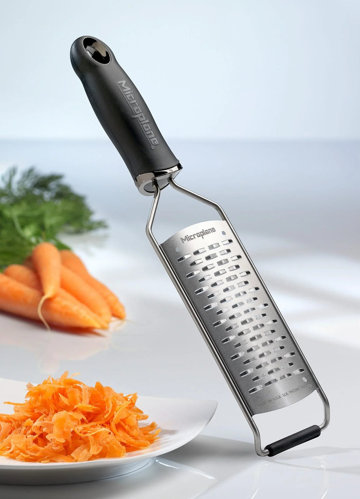 Microplane Gourmet rivejern medium ribbe med revne gulerødder på en tallerken