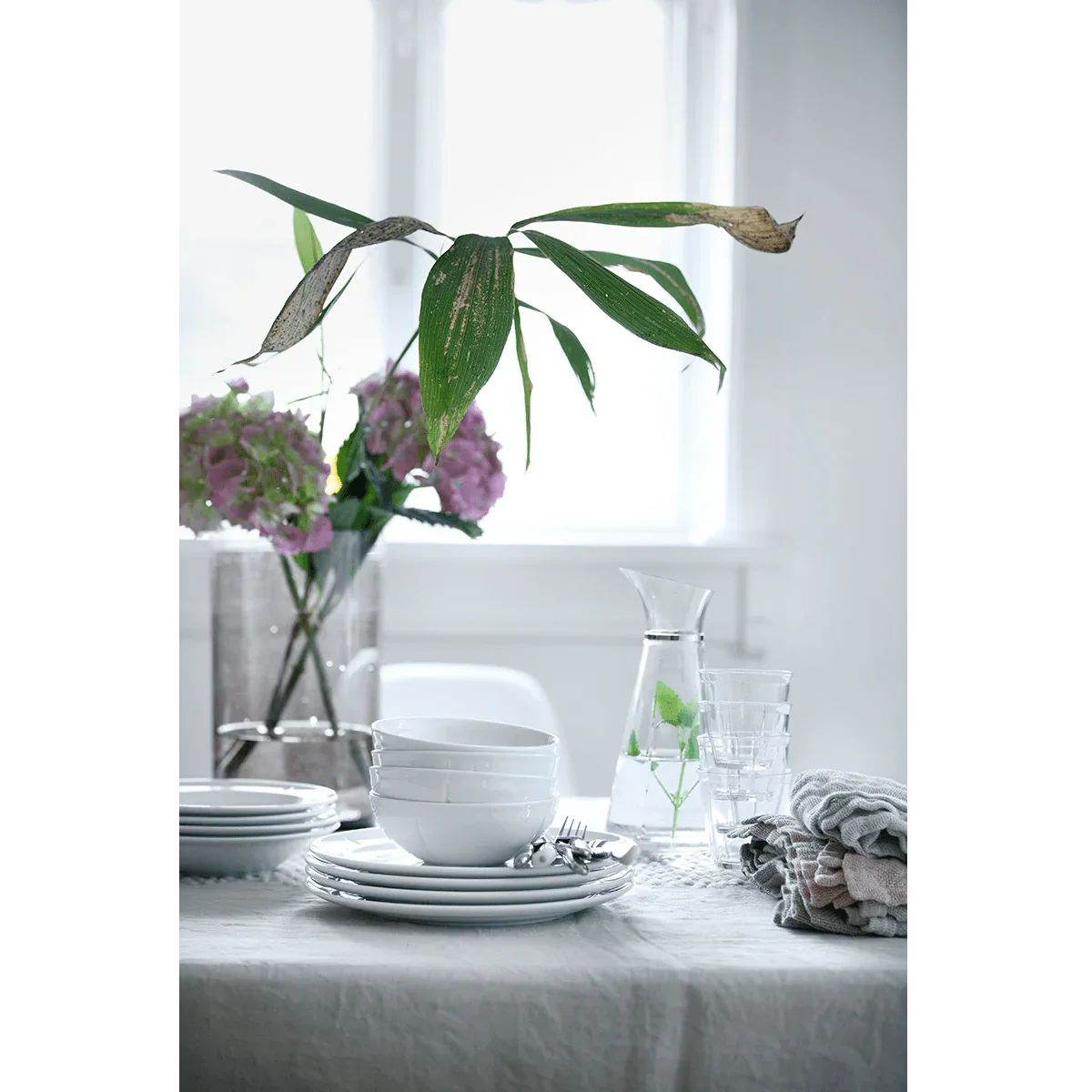 Hvide ROSENDAHL Grand Cru Soft dybe tallerkener og skåle på et dækket bord med blomster.
